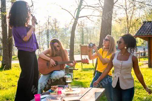 Visualização: Quatro amigos cantando, tocando violão, tirando fotos e fazendo um piquenique no parque