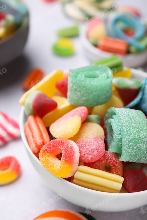 Preview: Bowl of tasty colorful jelly candies on white table, closeup