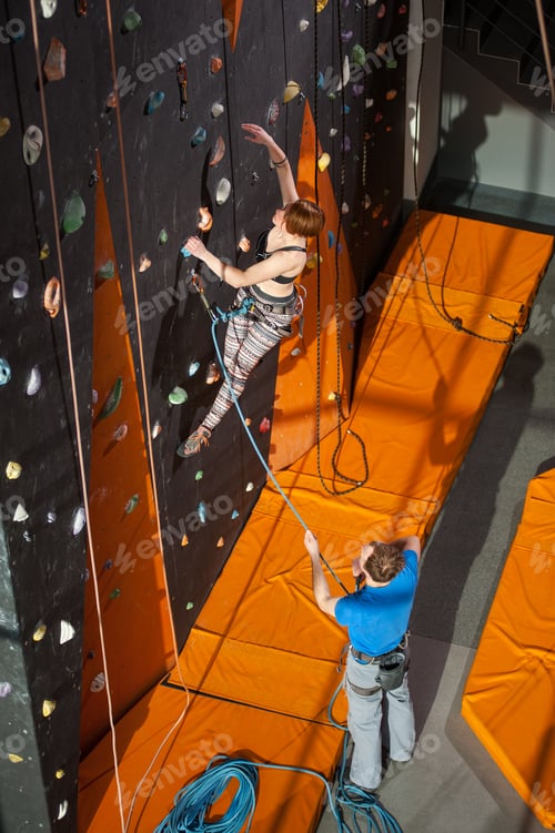 Preview: Female climber is climbing up on indoor rock-climbing wall