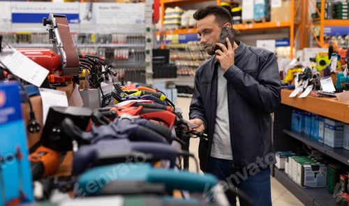 Preview: a male customer in a hardware store talking on the phone next to a rack of angle grinders