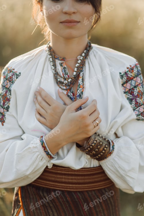 Preview: Young woman in traditional national embroidered shirt and skirt on nature at sunset.