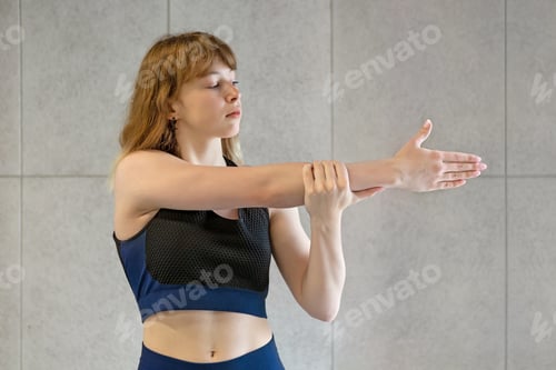 Preview: Portrait of a fitness pretty girl stretching hands against the background of the of the gym wall