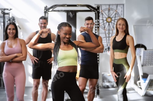 Preview: African fitness woman posing with biceps with a group of fitness people of different ethnicities.