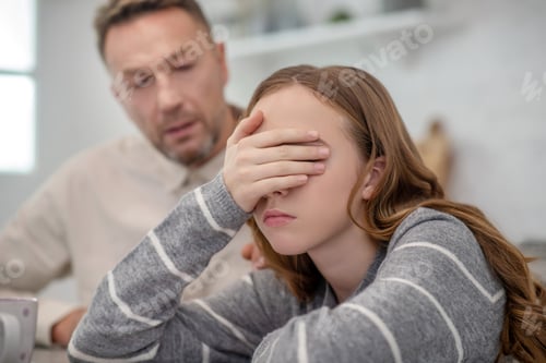 Preview: Long-haired girl in grey shirt closing her eyes with her hand