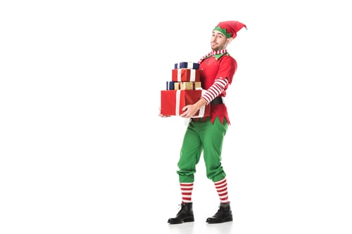 Preview: man in christmas elf costume looking at camera and carrying pile of presents isolated on white