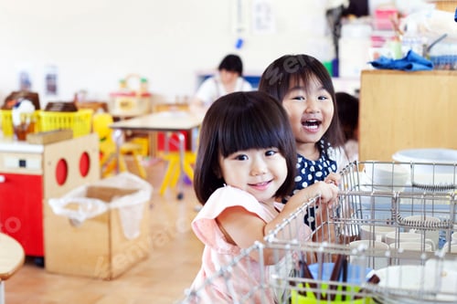 Preview: Two smiling girls in a Japanese preschool, looking at camera.