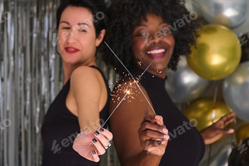 Preview: Two multiracial women dancing holding sparklers and celebrating New Year.
