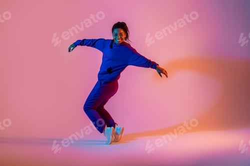 Preview: Street dance style. Happy black female hip-hop dancer dancing in neon pink lights, studio background