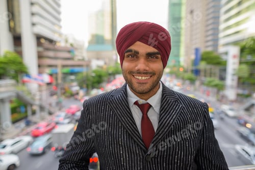 Preview: Happy Indian businessman with turban smiling outdoors in city