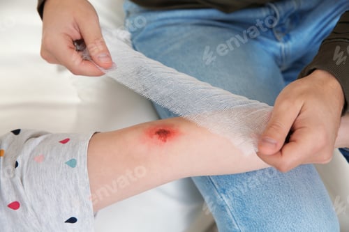 Preview: Father applying bandage on daughter's injured knee at home, closeup. First aid