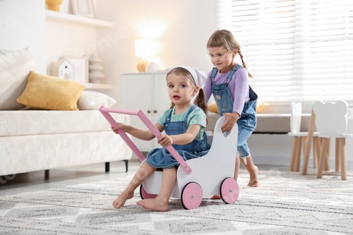 Preview: Cute little sisters playing with toy stroller at home