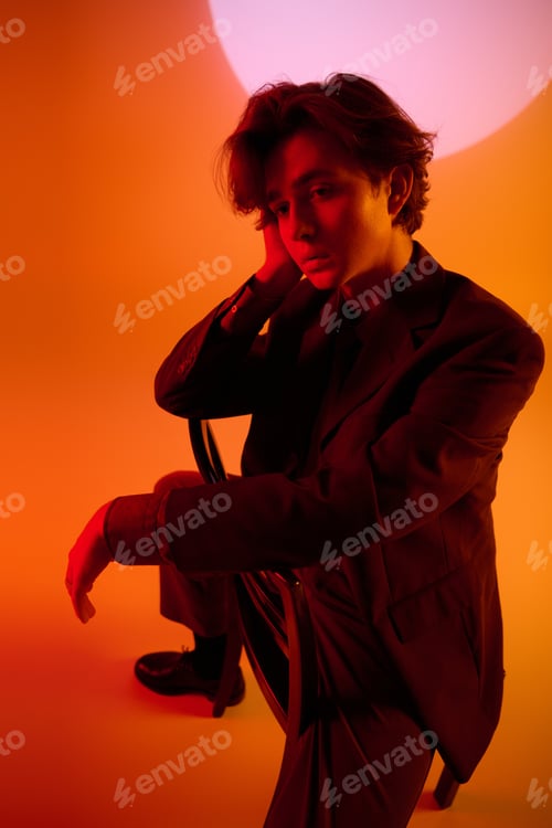 Preview: Stylish young man creating an artistic pose against a vibrant orange backdrop