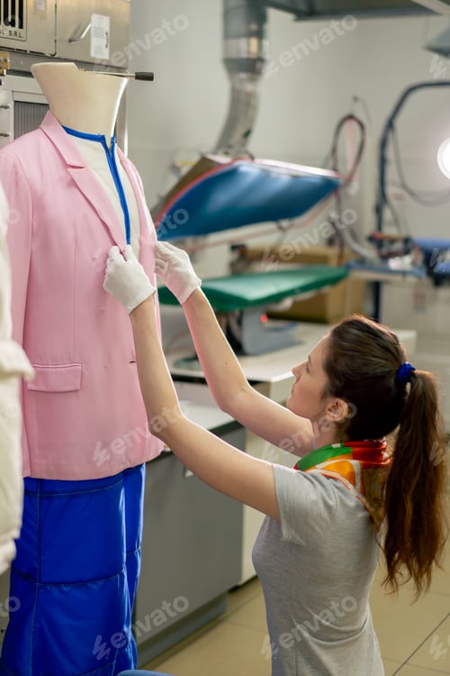 Preview: professional dry cleaner young girl takes a suit out of the dryer for finishing by hand press