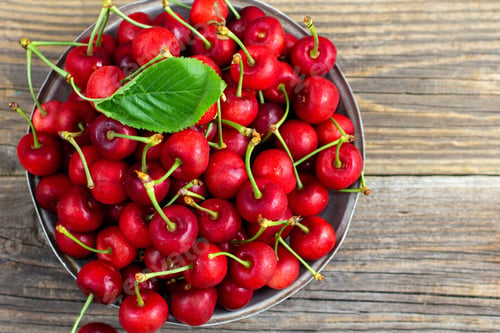 Preview: Ripe sweet cherries with green leaves in a metal plate on wooden background