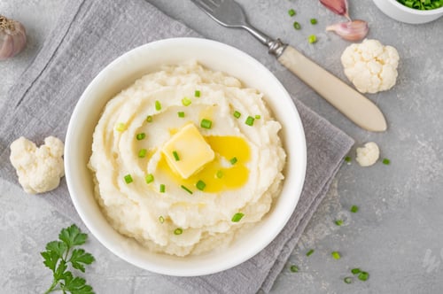 Preview: Cauliflower puree with butter and green onions in a white bowl. Healthy food. Copy space.