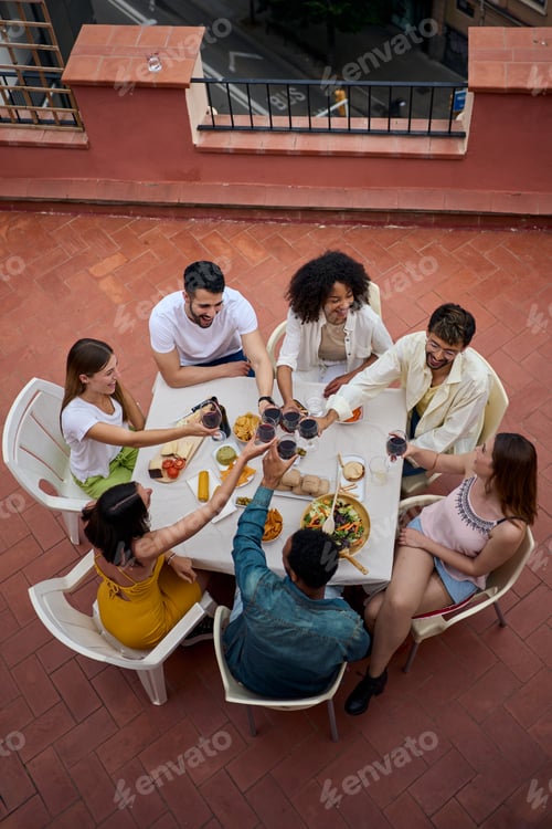 Preview: From above photo of young diverse friends toasting glasses red wine celebrating lunch rooftop.
