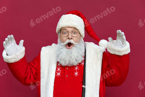 Preview: Amazed shocked funny Santa Claus wearing costume isolated on red background.