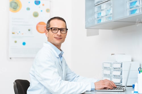 Preview: side view of doctor in white coat working on laptop at workplace in clinic