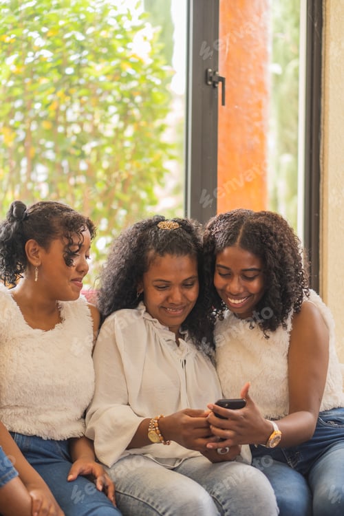 Preview: Optimistic Indian mother with teenage daughters surfing internet on cellphone while sitting