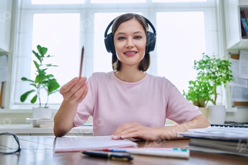 Preview: Webcam portrait of young female student wearing headphones, sitting at home at desk