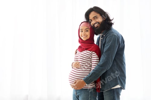 Preview: Portrait Of Pregnant Muslim Couple Embracing Near Window At Home