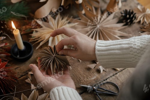 Preview: Making paper Christmas stars. Hands holding handmade star from craft paper on rustic background