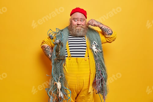 Preview: Photo of bearded sailor man curls mustache and poses indoor with fishing gears poses against yellow