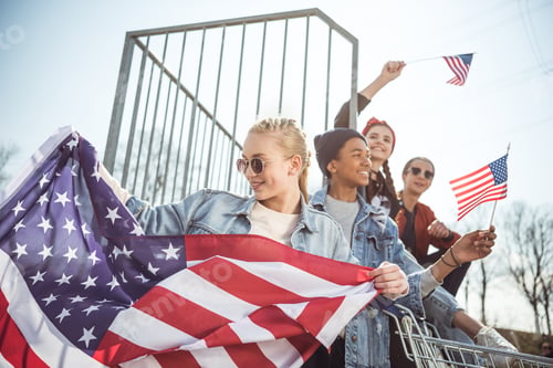 Preview: Happy teenagers group having fun and waving american flags at sunset