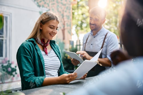 Preview: Young woman reading a menu while being with her friends in a cafe.