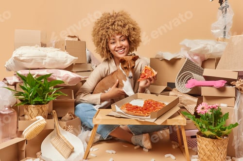 Preview: Cheerful European female house owner poses with pedigree dog eats tasty pizza prepars to housewarmin