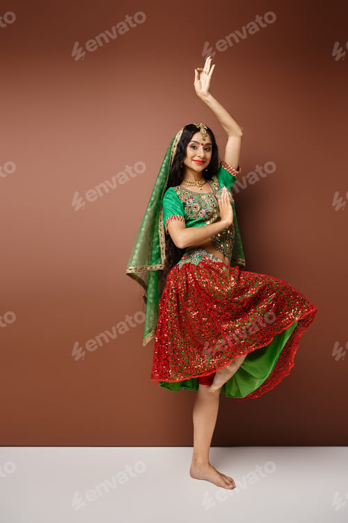 Preview: vertical shot of jolly young indian woman in national costume dancing lively and looking at camera