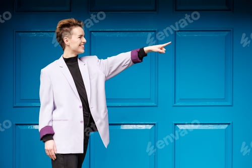 Preview: Happy alternative female model is pointing in front of blue door.