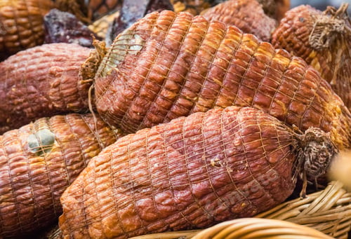 Preview: Fresh prepared smoked hams with spices in wicker basket on market stall