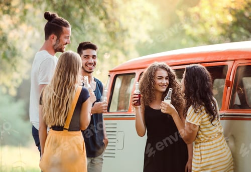 Preview: A group of friends standing outdoors on a roadtrip through countryside, holding bottles.