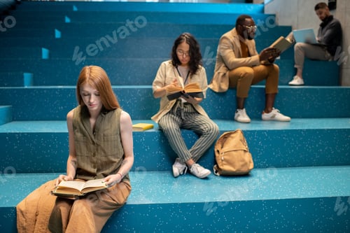 Preview: Group of intercultural students sitting on blue staircase and reading