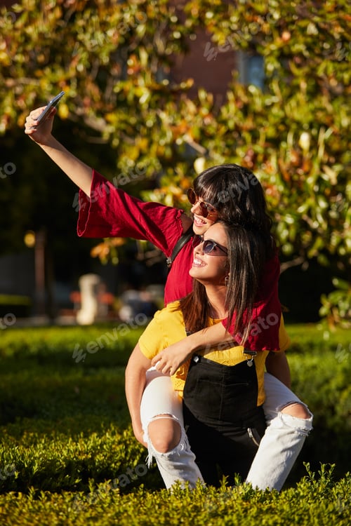 Preview: Two teenager girls taking a selfie while piggyback.