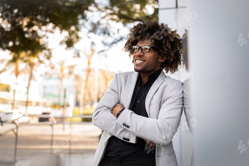 Preview: Confident black male entrepreneur posing with crossed arms and looking aside, walking near office