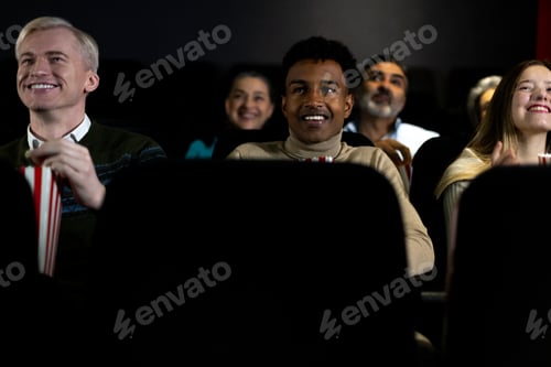 Preview: Diverse audience enjoying movie at cinema with popcorn