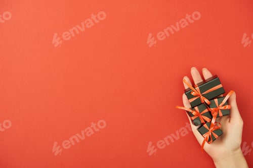 Preview: partial view of woman holding decorative black gift boxes in hand on red background with copy space