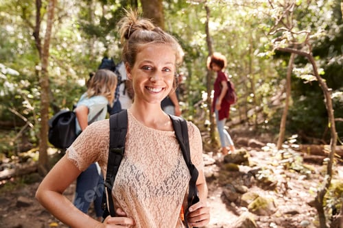 Preview: Portrait of millennial white woman with tied up hair hiking in a forest with her friends, close up