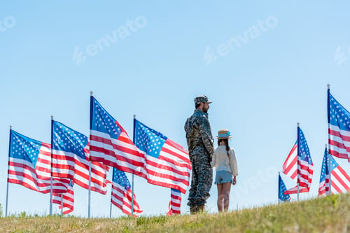 Preview: man in military uniform standing with daughter near american flags