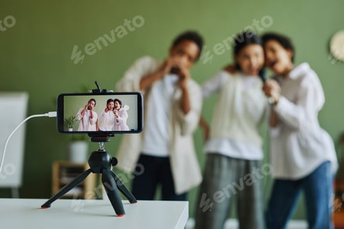 Preview: Screen of smartphone on tripod with three schoolkids performing song together