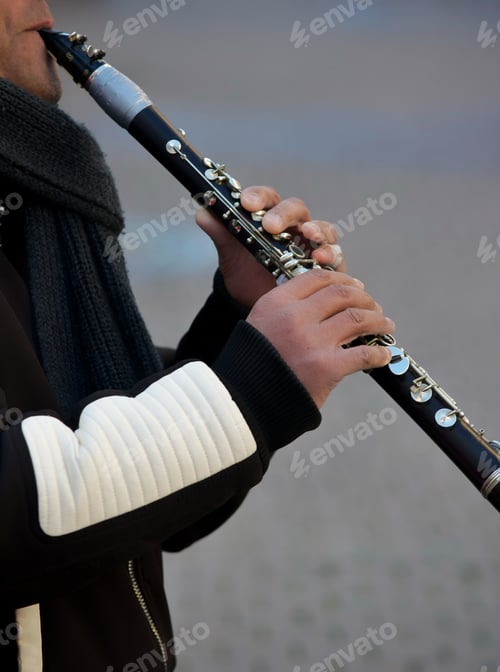 Preview: A diverse unrecognizable street musician plays music on a clarinet outside on a cold winter day