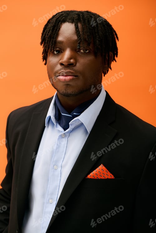 Preview: Handsome young man in stylish attire poses confidently against a vibrant orange backdrop