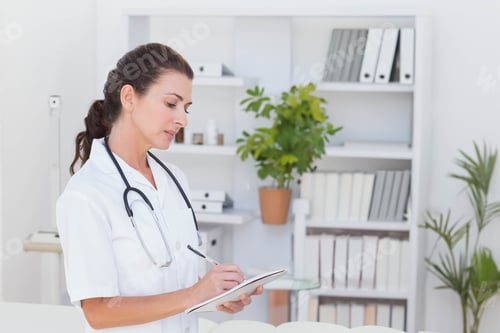 Preview: Stethoscope resting beside clipboard and pen on glass-top table in clinical office with greenery