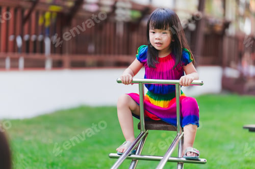 Preview: Asian child in colorful dress playing seesaw in the laws playground at outdoors.