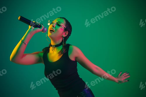 Preview: Caucasian female singer portrait isolated on green studio background in neon light