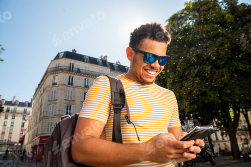Preview: happy young african american man with bag looking at phone in city