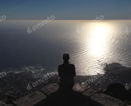 Preview: View from behind woman sitting on the edge overlooking the ocean
