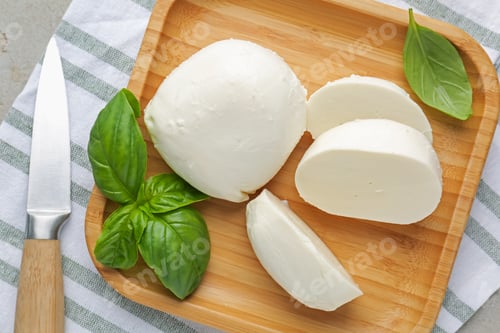 Preview: Pieces of delicious mozzarella cheese, basil leaves and knife on grey table, top view